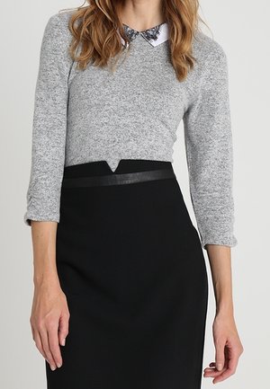 Grå stickad tröja med trekvartslånga ärmar och vit krage; ihop med en svart blyertskjol med läderdetalj vid midjan.