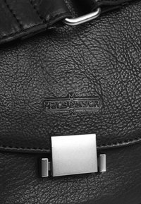 Dettaglio di uno zaino in pelle nera con un gancio metallico argento e logo del marchio impresso. La pelle presenta una finitura texturizzata a granuli.