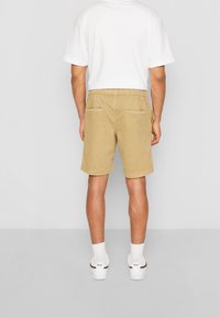 Shorts kaki en coton avec une coupe décontractée, une ceinture élastique, deux poches arrière et un ourlet retroussé, associés à un T-shirt blanc et des chaussettes.