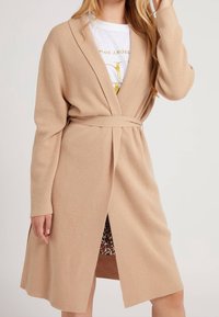 Beiger, gestrickter Cardigan mit Gürtel, offener Front, langen Ärmeln und seitlichen Schlitzen, die ein Futter mit Leopardenmuster zeigen.