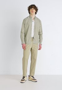 Hellgrünes Langarmhemd mit Knöpfen, kombiniert mit hellen beigen Hosen und Sneakers mit braunen Akzenten. Schlichte Textur und taillierte Passform.