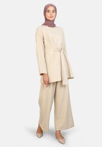 Beige linen outfit featuring a long-sleeve wrap top with a side knot and wide-leg pants. Completed with a light-colored flat shoe.