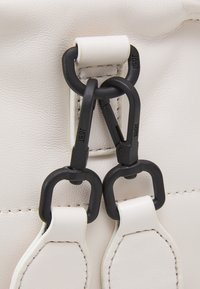 Gros plan de fermoirs métalliques noirs fixés à des lanières en cuir blanc sur une surface en cuir blanc texturée.