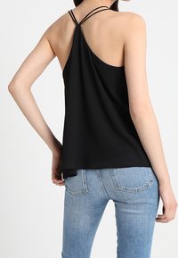 Top in cotone nero con scollatura bassa e spalline sottili, abbinato a jeans azzurri chiari con design classico a cinque tasche.