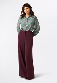 Bluse in Petrol mit floralem Muster und Knopfleiste, kombiniert mit hoch taillierten, weit geschnittenen bordeauxfarbenen Hosen, die eine lockere Passform und eine glatte Textur bieten.