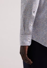 Camicia a maniche lunghe di colore azzurro chiaro con un motivo floreale nei toni del rosa e del bianco. Presenta polsini con bottoni e un piccolo dettaglio ricamato sulla manica.