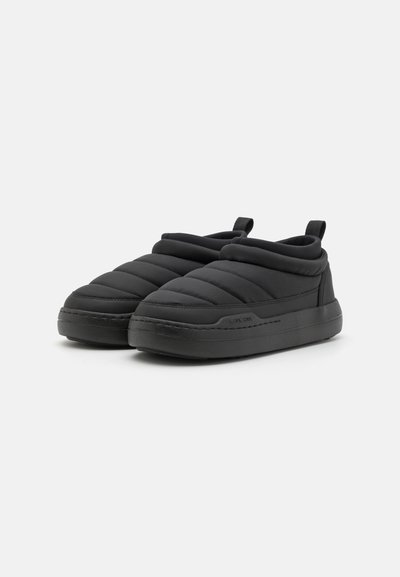 Chaussures noires en tissu matelassé à enfiler, avec un design rembourré, des semelles en caoutchouc et de petites languettes à l'arrière pour un enfilage facile. Texture lisse sur toute la surface.