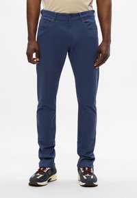 Niebieskie spodnie z bawełny z prostym krojem, posiadające kieszenie z przodu, szlufki na pasek i średni stan. Połączone z wielokolorowymi trampkami.