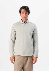 Light gray button-up shirt with a textured finish, featuring a folded collar and a small embroidered logo on the chest.