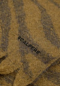 Bufanda a rayas marrón y gris hecha de tejido suave y texturizado, con el texto "SCALPERS" en negro. Los bordes con flecos completan el diseño.