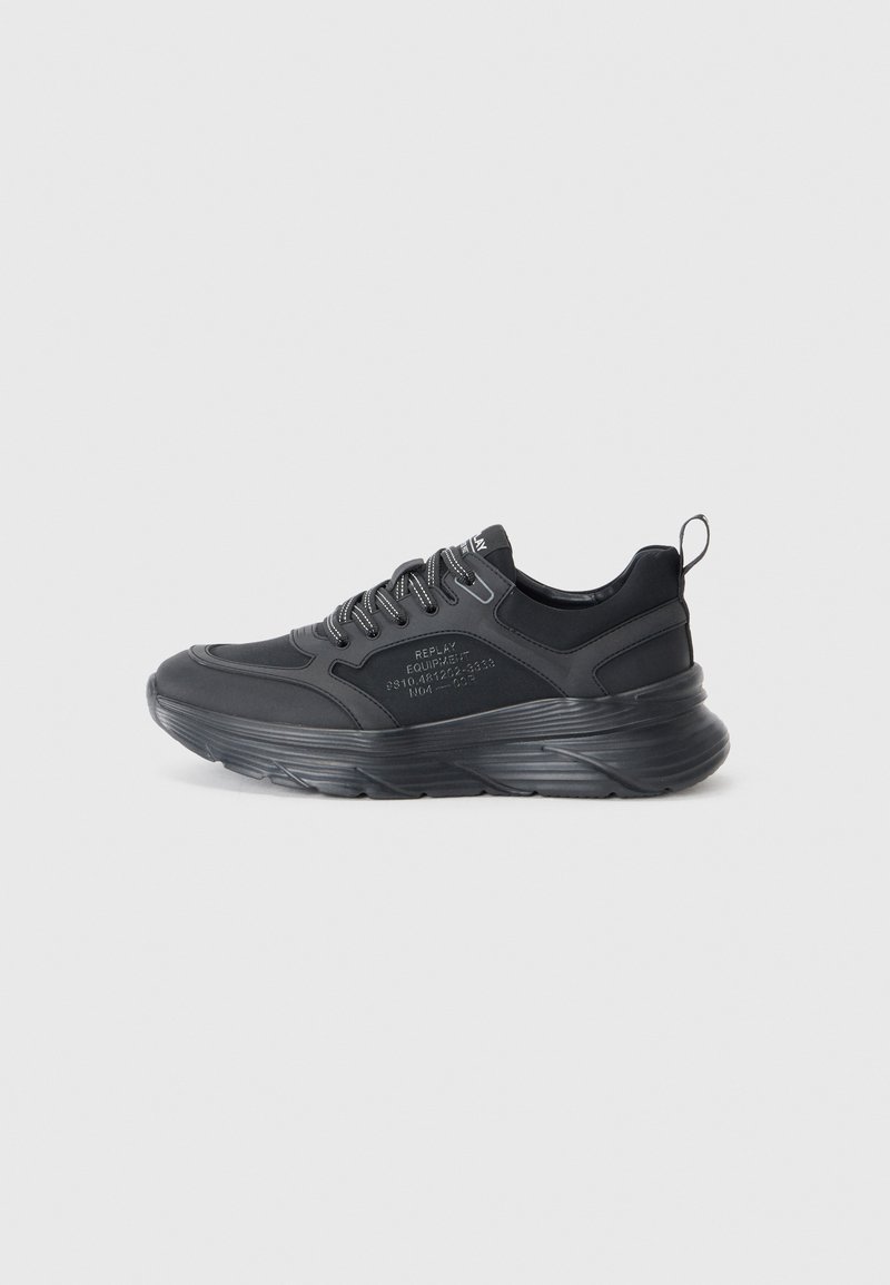 Chaussures de sport noires avec une tige en synthétique texturé, une semelle rembourrée proéminente et des lacets réfléchissants. Présente un logo sur le côté.