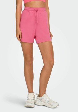 Rosa Baumwollshorts mit elastischem Bund und Kordelzug. Glatte Textur, lockere Passform und gesäumte Bündchen. Kombiniert mit weißen Sneakers.