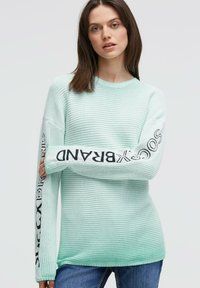 Mintgrüner Strickpullover mit einer strukturierten Optik, schwarzem Markenschriftzug entlang eines Arms und einem lockeren Schnitt.