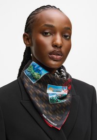 Kvinne med flettede hår har på seg en svart blazer og et mønstret Karl Lagerfeld skjerf med reisetema-om Monaco.