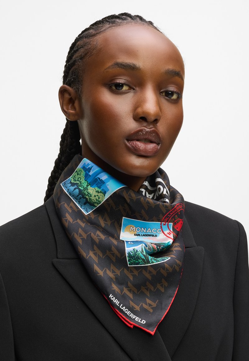 Kvinne med flettede hår har på seg en svart blazer og et mønstret Karl Lagerfeld skjerf med reisetema-om Monaco.