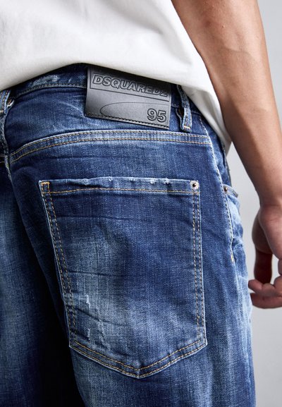 Tumed sinised teksad, millel on kulumise detailid, tagumisel vöökohal on nahklabel "DSQUARED2 95". Lihtne viie tasku disain.
