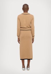 Beige strikket to-dels sett med langermet topp med krage og lang skjørt, aksentuert med svart kant ved nederkant og midje.