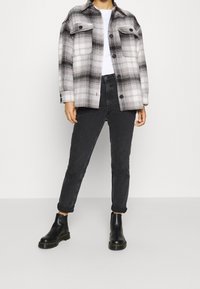 Black and white checked shirt jacket, two chest pockets, paired with black slim jeans and black ankle boots, smooth texture overall.