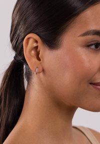 Silberne Creolen mit einer Reihe kleiner klarer Kristalle, eingefasst in poliertem Metall. Am Ohr eines Models getragen, das das filigrane Design zur Schau stellt.