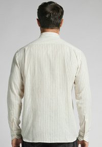 Langarmshirt van off-white stof met subtiele verticale strepen. Voorzien van een standaardkraag en knoopsluiting bij de manchetten, met een relaxte pasvorm.