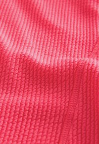 Getextureerde stof in felroze kleur, met een ribbelpatroon met verhoogde details en een gladde, zachte textuur.