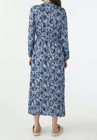 Långärmad blå klänning med blommönster, elastisk midja och ankellängd. Bärs med ljusbeige skor.