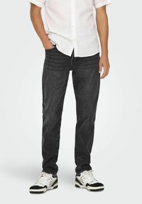 Jean slim de mezcla de algodón negro, combinados con una camisa blanca de manga corta y zapatillas en blanco y negro. Diseño simple, sin patrones visibles.