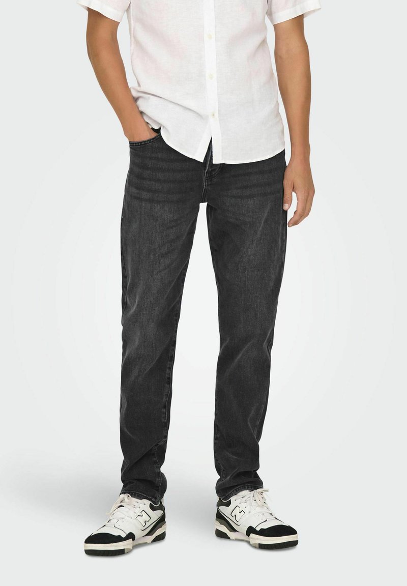 Jean slim de mezcla de algodón negro, combinados con una camisa blanca de manga corta y zapatillas en blanco y negro. Diseño simple, sin patrones visibles.