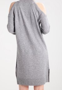 Robe grise en maille avec design à épaules découvertes, tissu texturé, col et ourlet côtelés, fentes latérales pour faciliter les mouvements.