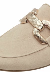 Chaussure slip-on en suède beige avec un accent décoratif en chaîne métallique dorée sur le dessus, dotée d'un bout rond et d'une surface texturée.
