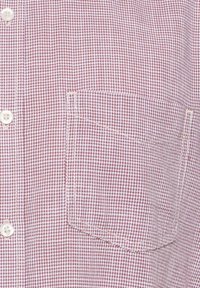 Camisa de manga corta con un patrón de cuadros en colores marrón y blanco, con un único bolsillo y botones blancos. Tejido texturizado.