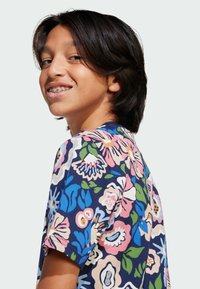 Floral short-sleeve shirt featuring a navy background with colorful flower patterns in pink, blue, and green. Soft fabric and relaxed fit.