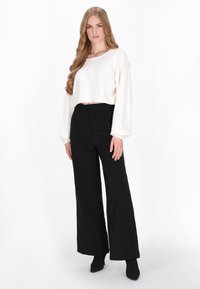 Pull blanc court à manches longues, associé à un pantalon large taille haute noir. Texture lisse, taille ajustée et détails subtils.