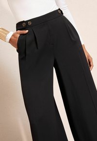 Černé široké kalhoty s vysokým pasem, puky a dvěma předními knoflíky. Vyrobené z hladké látky se bočními kapsami.