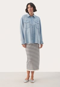 Světle modrá denimová oversized košile se dvěma náprsními kapsami, v kombinaci s bílým pruhovaným sukní do půlky lýtek a stříbrnými botami na slip-on.