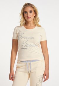Cremfarbendes T-Shirt mit kurzen Ärmeln und grauem Text, kombiniert mit passenden Jogginghosen mit Kordelzug und dekorativen Akzenten.