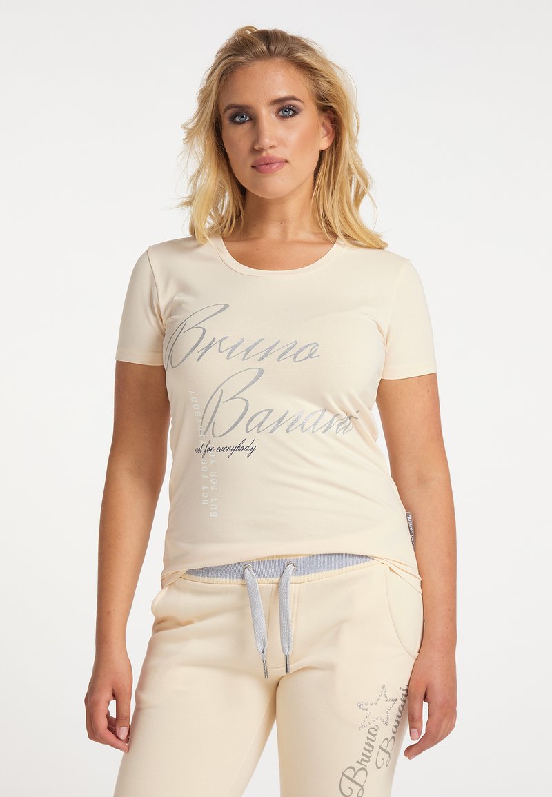 Cremfarbendes T-Shirt mit kurzen Ärmeln und grauem Text, kombiniert mit passenden Jogginghosen mit Kordelzug und dekorativen Akzenten.