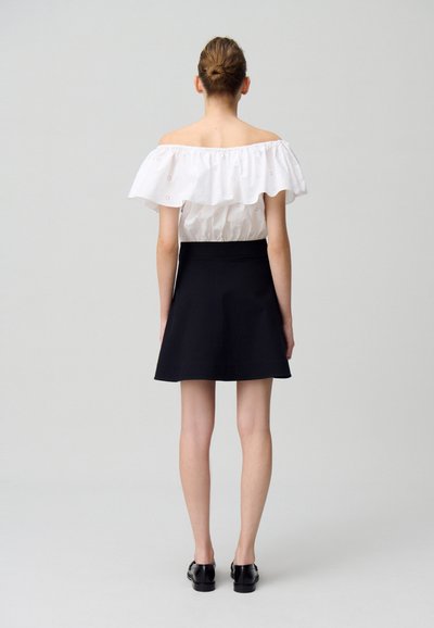 Haut blanc dénudé sur les épaules avec un col à volants, associé à une jupe évasée noire. Texture lisse, taille ajustée et coupe à mi-cuisse.