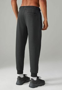 Zwarte sweatpants met een elastische band, taps toelopende broekspijpen,zijzakken en een gestructureerde stof, gecombineerd met donkere sneakers en witte sokken.