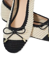 Beige and black crocheted ballet flats with a rounded toe, featuring a black bow accent and gold hardware. Smooth interior lining.