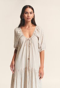 Gestreepte jurk in lichtbeige met blauwe en bruine verticale strepen, voorzien van een diepe halslijn, pofmouwen en een geplooide rok.