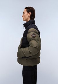 Pūkinis paltas su juoda viršutine dalimi ir alyvuogių žaluma apatinėje dalyje, su aukštu apykakle, užtrauktuku ir apvaliu logotipo ženkleliu ant rankovės.