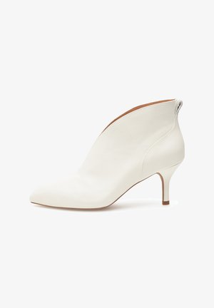 Bottes blanches en cuir, hauteur cheville, avec un bout pointu et un talon fin, présentant un design épuré et une texture lisse. Style minimaliste sans ornements.