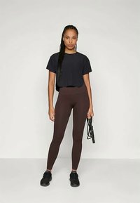 Must t-särk, ribased pruunid retuusid ja mustad tossud. Riietus on relaxitud lõikega ja minimalistik, sobides suurepäraselt spordirõivasteks.