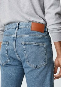 Vaqueros azul claro de mezclilla con cintura alta, que cuentan con un parche de cuero marrón, bolsillos traseros y una tela texturizada.