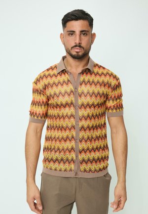 Chemise à manches courtes avec un motif en zigzag dans des couleurs orange, jaune et marron ; dotée d'un col beige et d'une fermeture à boutons sur le devant.