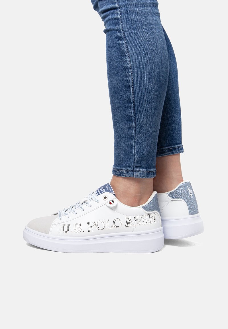 Białe sneakersy z niebieskimi akcentami brokatowymi, perforowanymi detalami oraz materiałowym językiem. Posiadają grubą białą podeszwę i tekst z logo po boku.