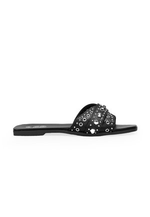 Sandalias negras de slide con tiras cruzadas adornadas con tachuelas plateadas y acentos circulares. Suela plana, textura suave y diseño minimalista.