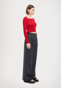 Red ribbed crop top with long sleeves, paired with high-waisted, wide-leg gray trousers and black platform sandals with buckle details.