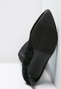 Stivaletto in pizzo nero con punta affusolata, tessuto testurizzato, suola in gomma piatta e sottili dettagli laterali per un design snello.